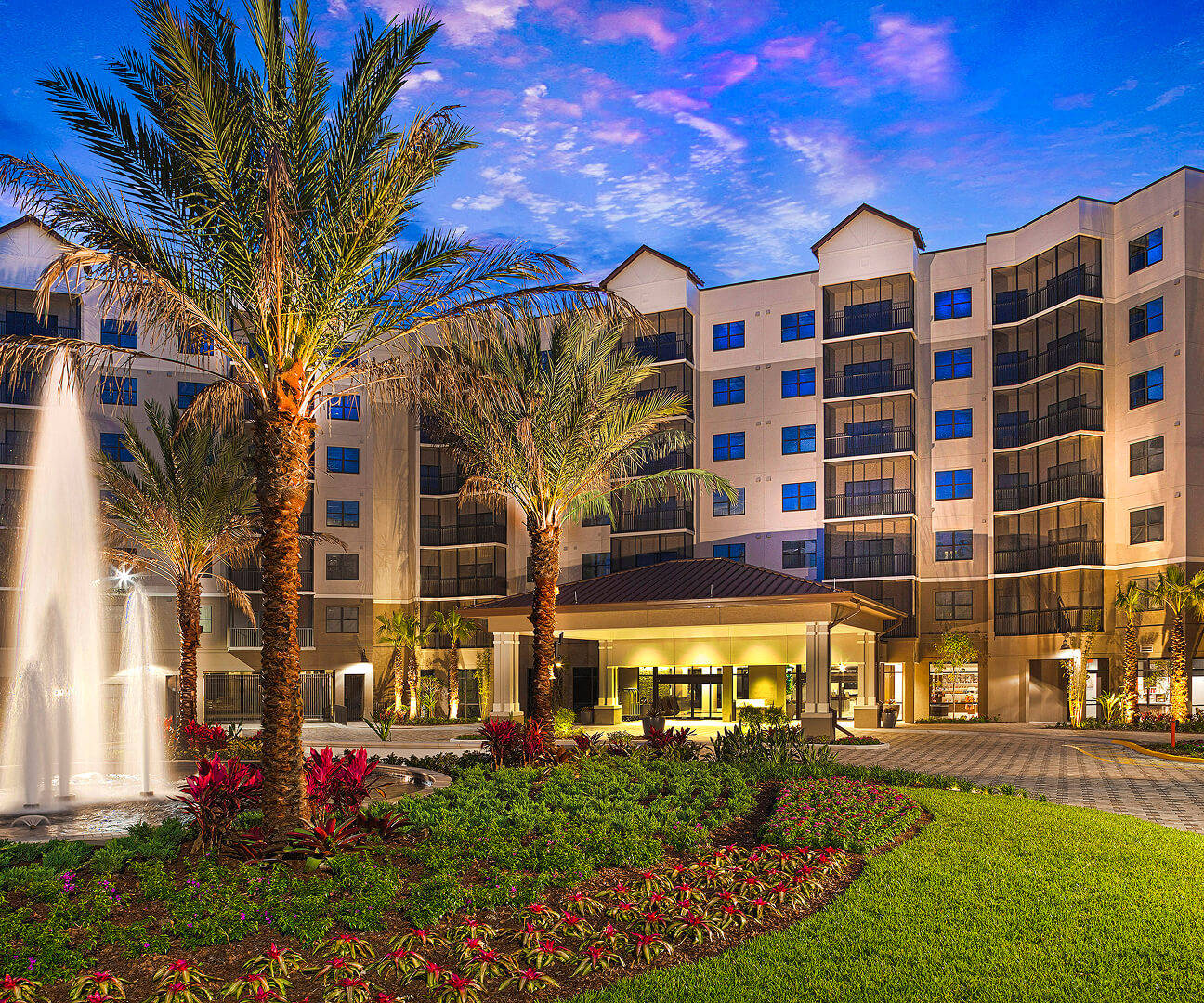 An exterior view of a hotel with a palm tree and fountain in front